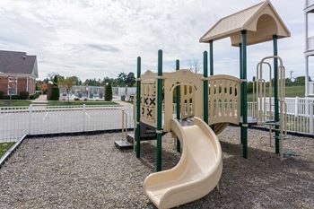 A playground with a yellow slide and a white fence.